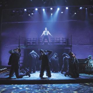bc体育演出音乐剧《春之觉醒》的场景, 一群穿着古装的演员跪在地上，一名男独唱者在一个高架平台上的蓝色聚光灯下唱歌.